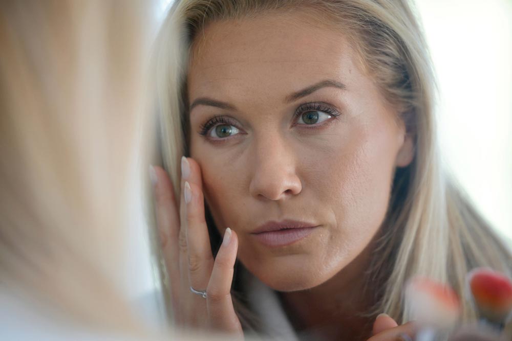 Middle-aged woman looking at her skin in front of mirror