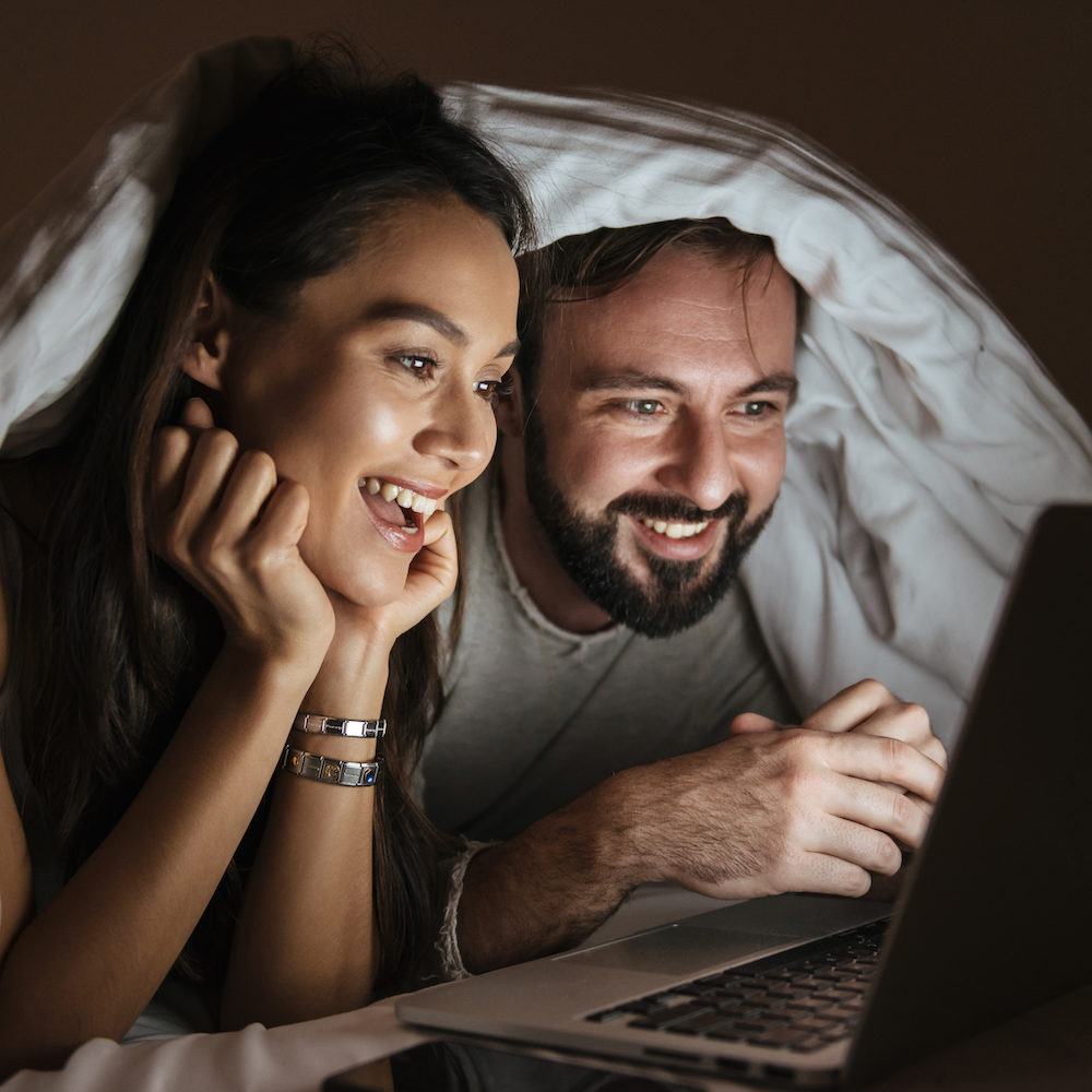 Couple watching a movie under a blanket smiling