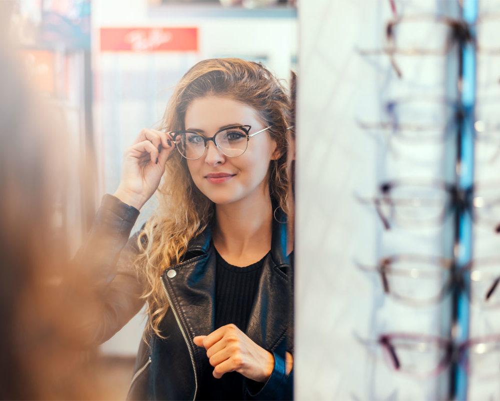 Woman examining new glasses in mirror at optometry office