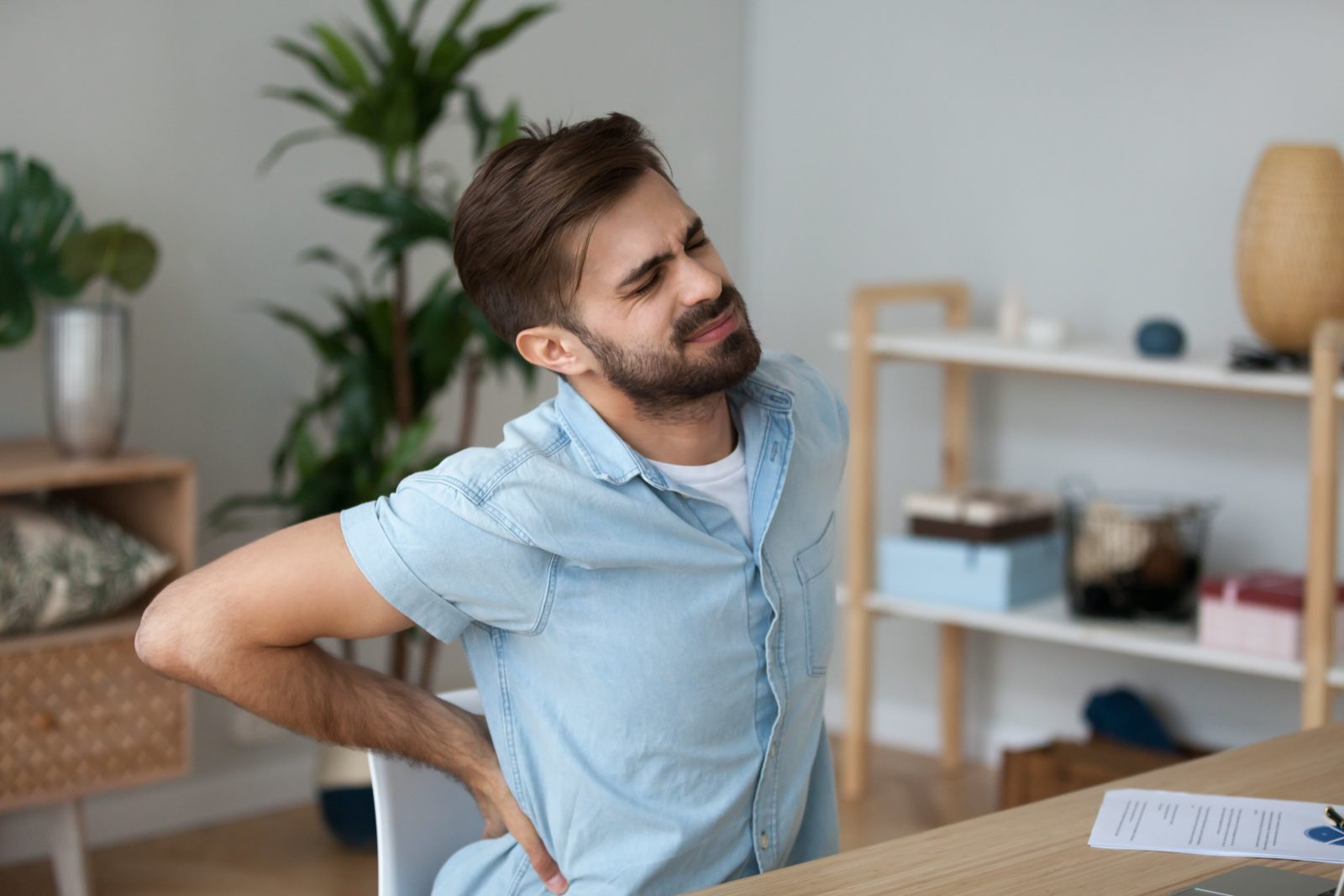 man sitting at desk wincing and holding his back in pain