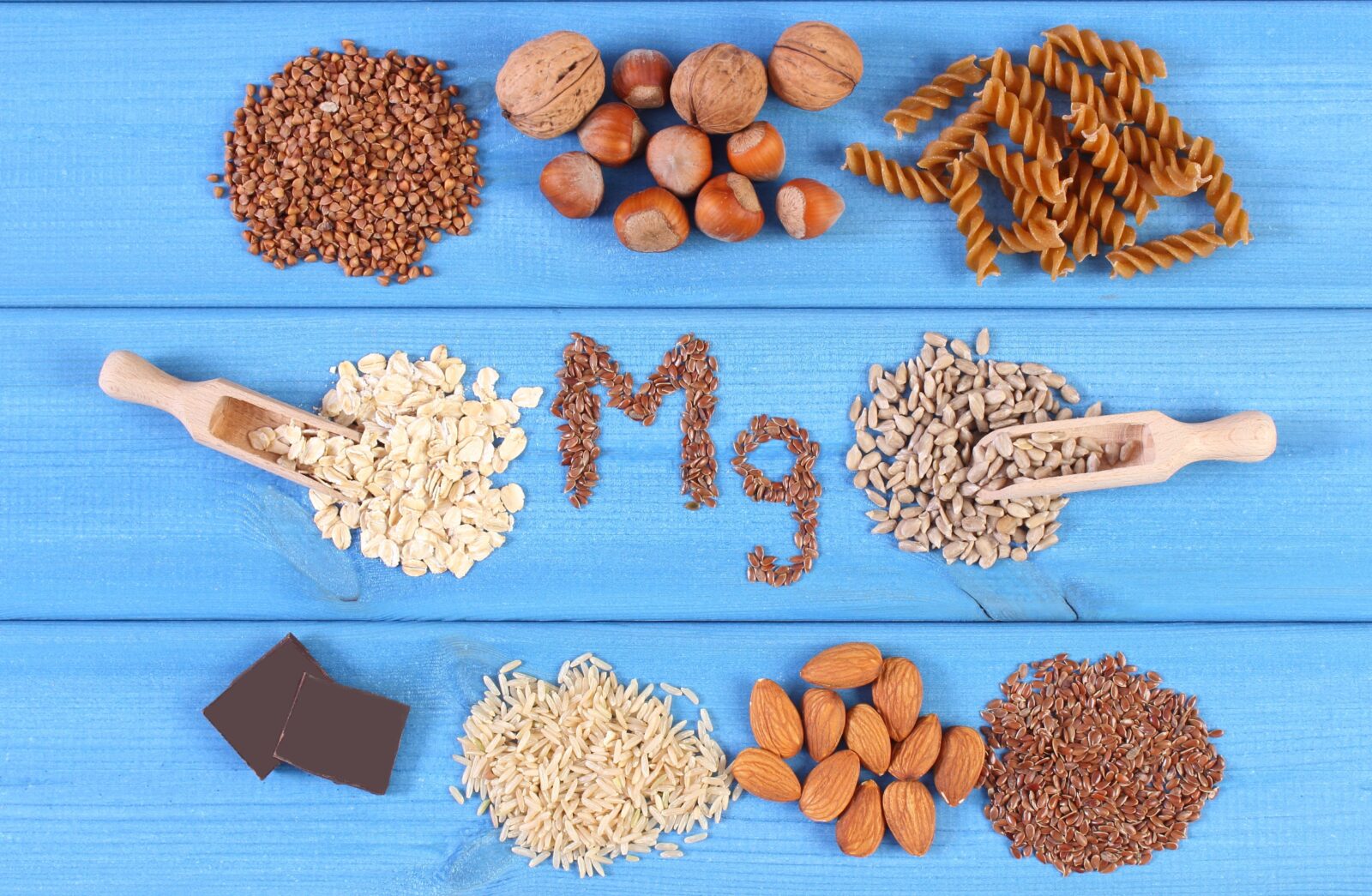Inscription Mg, ingredients and products containing magnesium and dietary fiber, healthy nutrition, wholemeal pasta, sunflower, buckwheat, oatmeal, brown rice, linseed, hazelnut, almonds, chocolate
