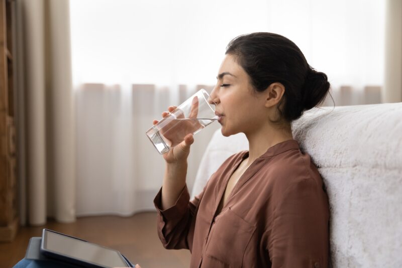 Side profile attractive young Indian woman holding glass and drink still water