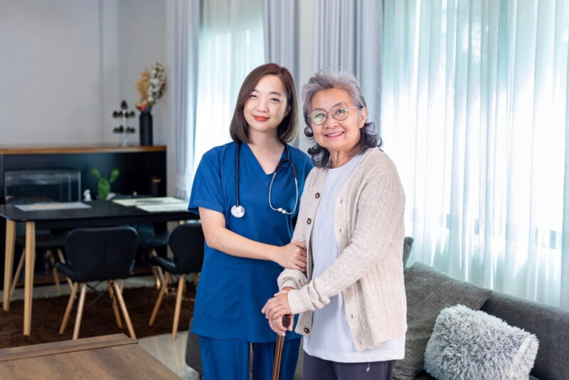 Senior woman get medical service visit from caregiver nurse at home while practice using walking cane or stick after knee surgery