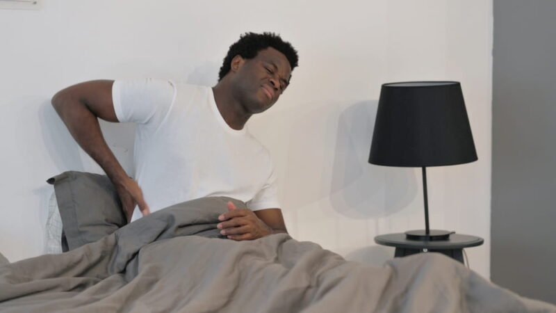 African Man with Back Pain while Sitting in Bed