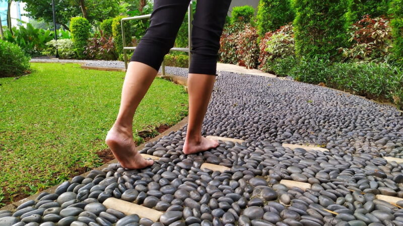 Bare feet woman walking on stepping stones for health, reflexology massage of foot nerves
