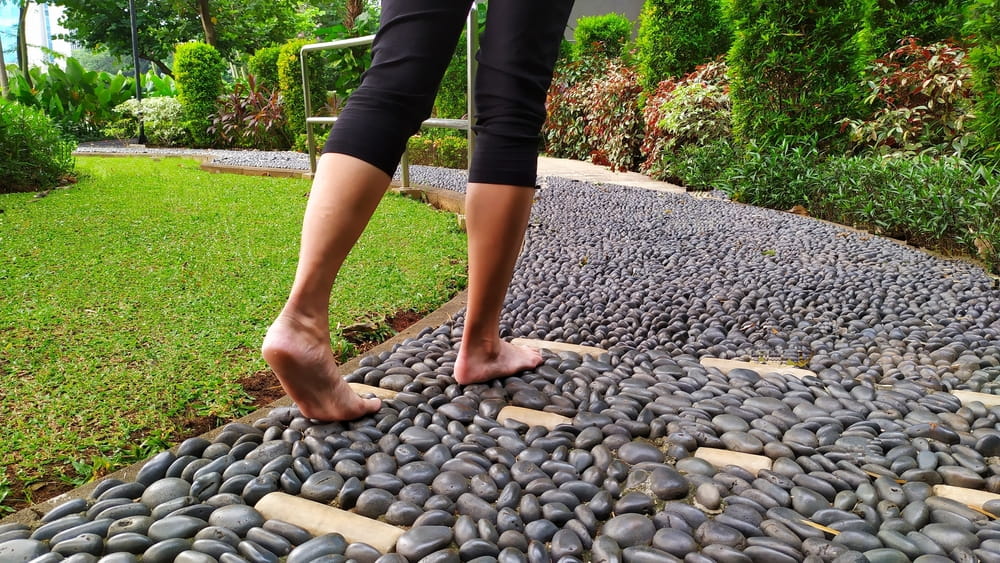 Bare feet woman walking on stepping stones for health, reflexology massage of foot nerves