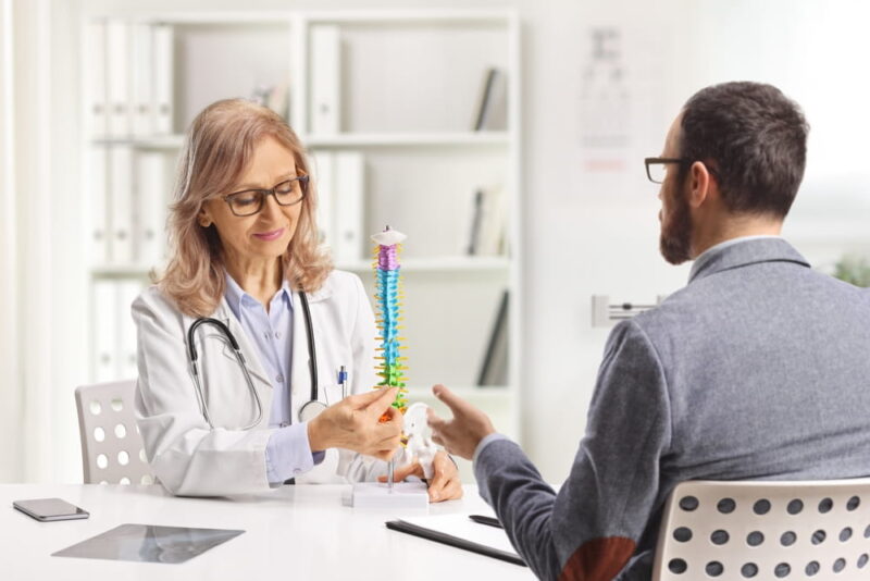 Man at a hospital appointment with an orthopedic doctor looking at a human spine model