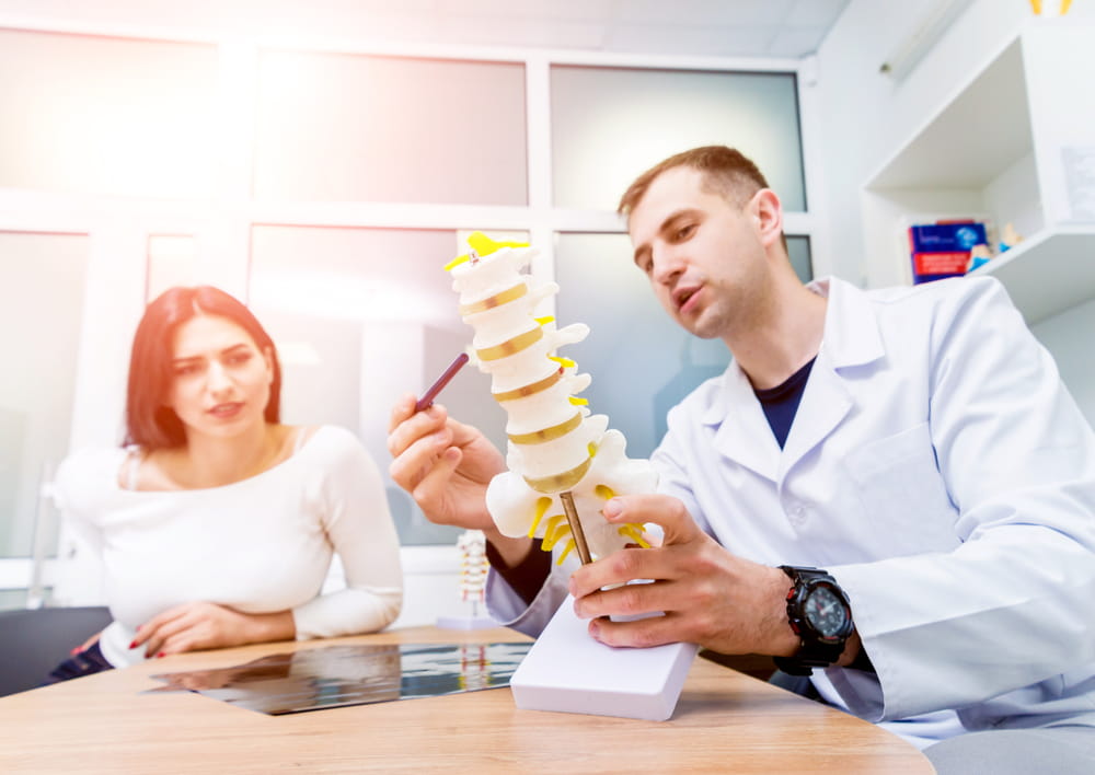 Orthopedist showing spine model to patient in hospital. Medical background