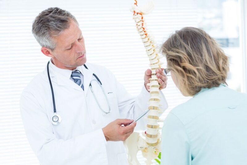 Doctor pointing anatomical spine in medical office