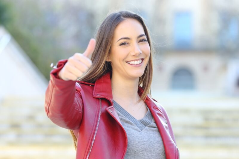 Front view portrait of a happy woman in red gesturing thumb up outside in the street