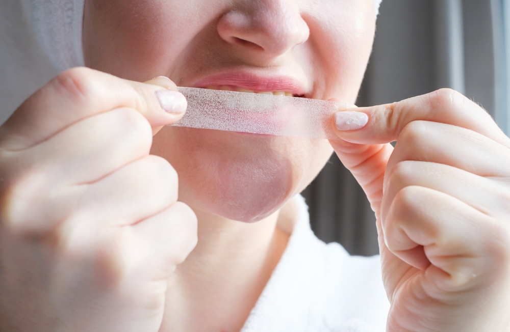 Portrait of a young woman holding a whitening strip for teeth, close up.