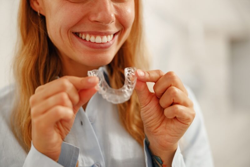 A joyful woman holds up her clear dental aligner, proudly displaying her confident and radiant smile