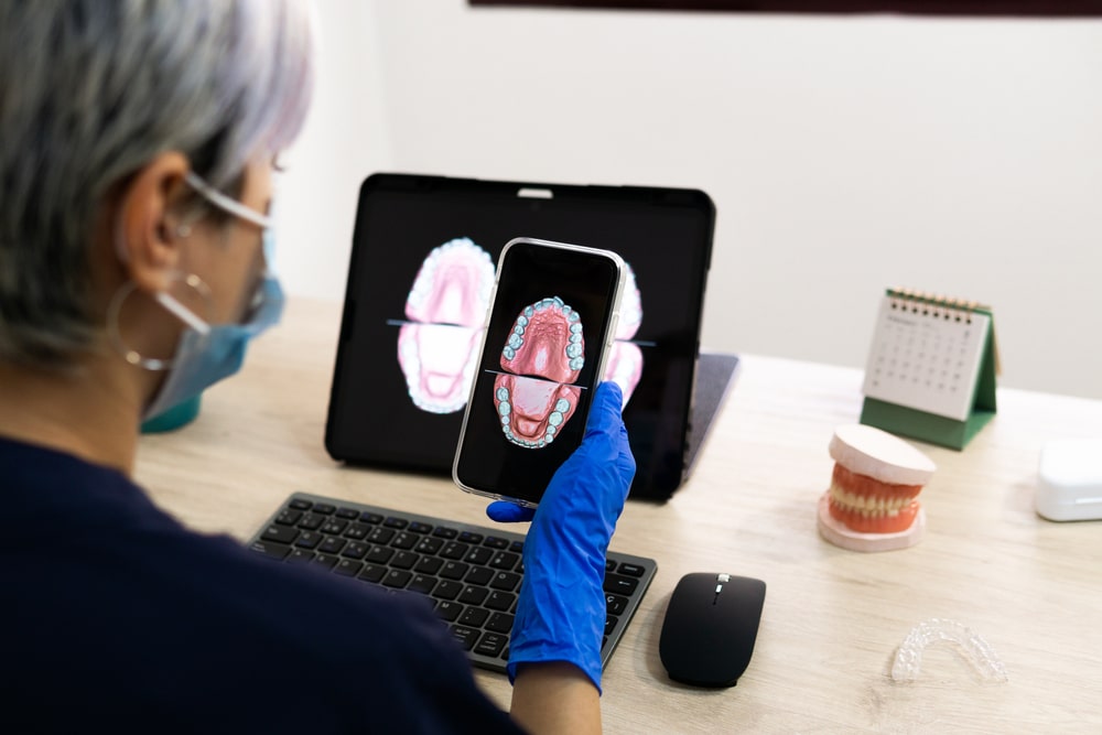 Dental technician looking at the mobile while designing a new dental prosthesis with his computer in the laboratory