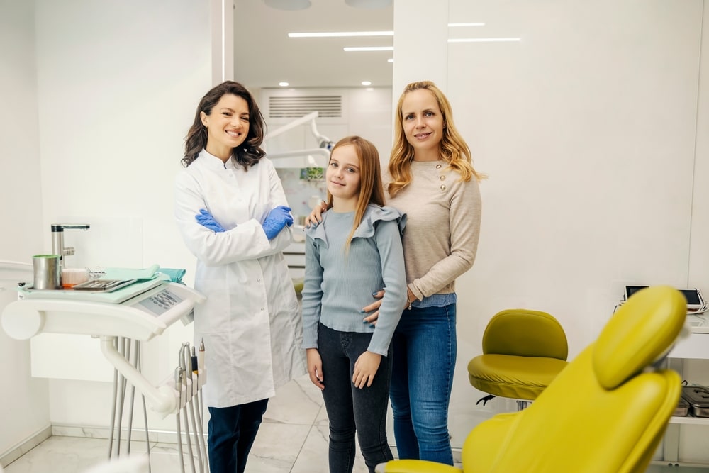 A mother and her daughter visiting dentist at dentist office and smiling at the camera.