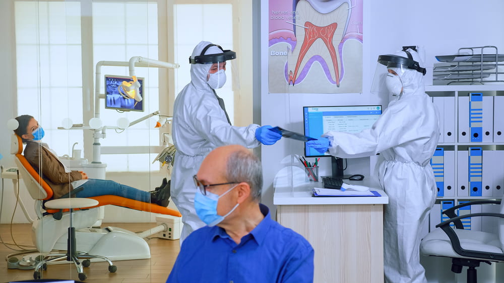 Stomatologist in protective suit asking for patient dental x-ray examining teeth problems during coronavirus pandemic in modern clinic.