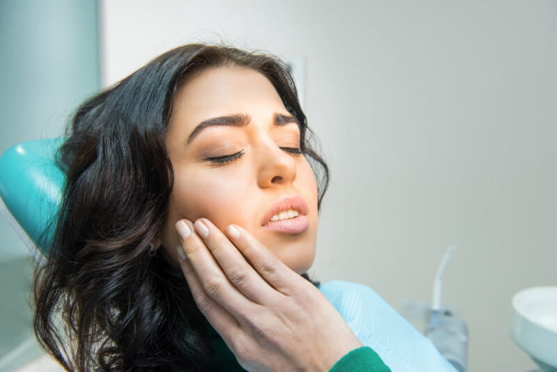 Young woman having toothache. Sad lady at the dentist. Gum disease symptom.