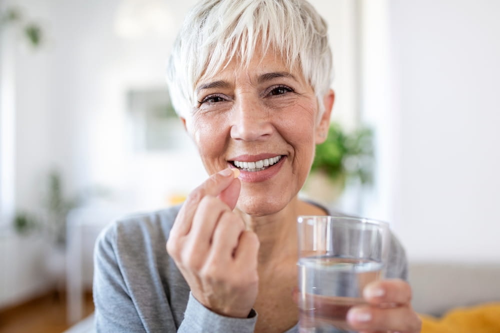 Head shot portrait happy woman holds pill glass of water