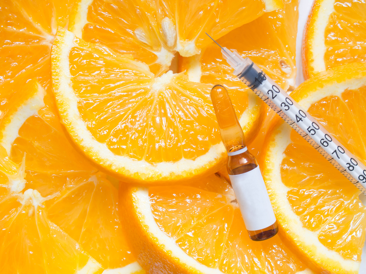 High dose vitamin C brown ampule for injection with syringe on fresh juicy orange fruit slides