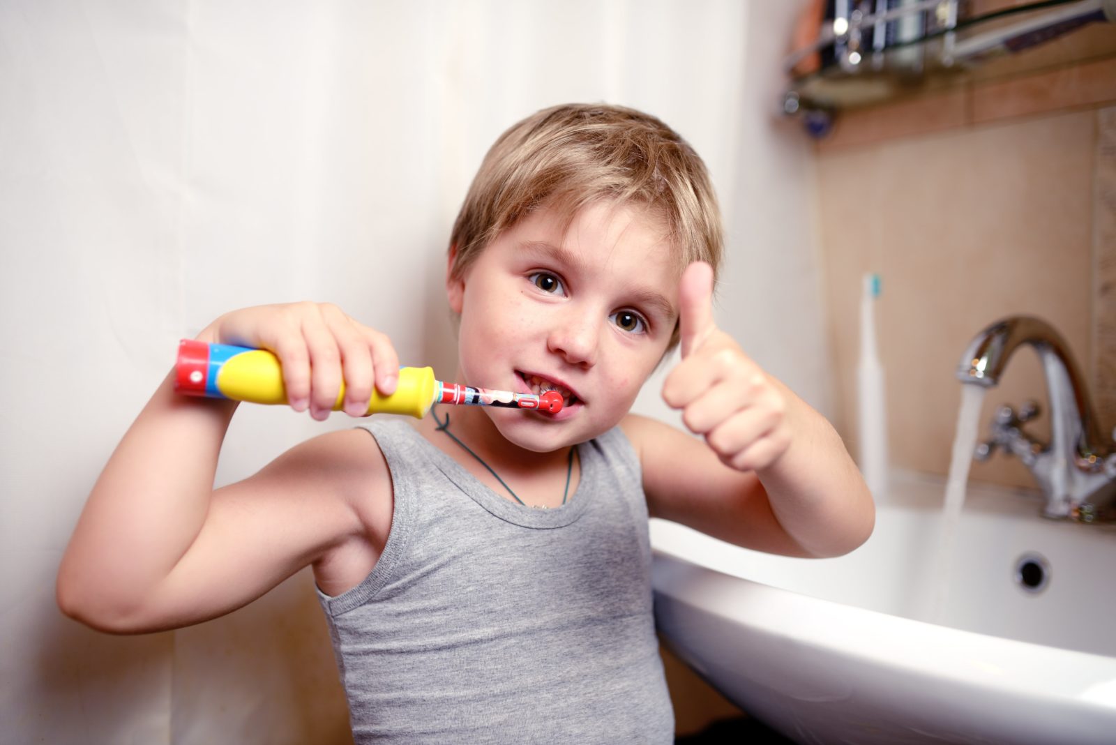 young boy brushing his teeth with a thumbs up
