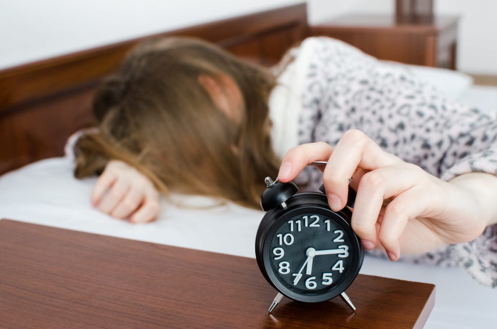 teen girl facedown pressing snooze on her alarm clock