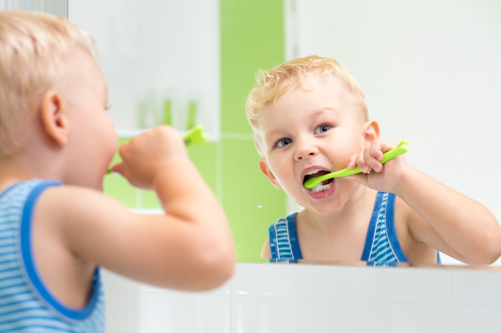 toddler boy brushing his teeth in the mirror