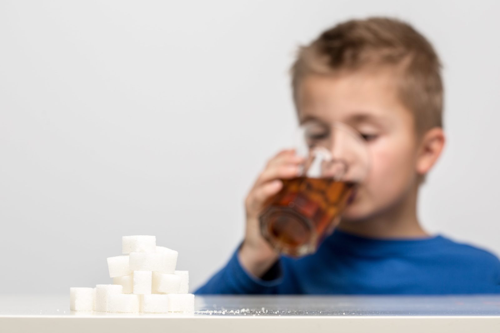 a pile of sugar cubes in focus with a blurred child drinking soda in the background