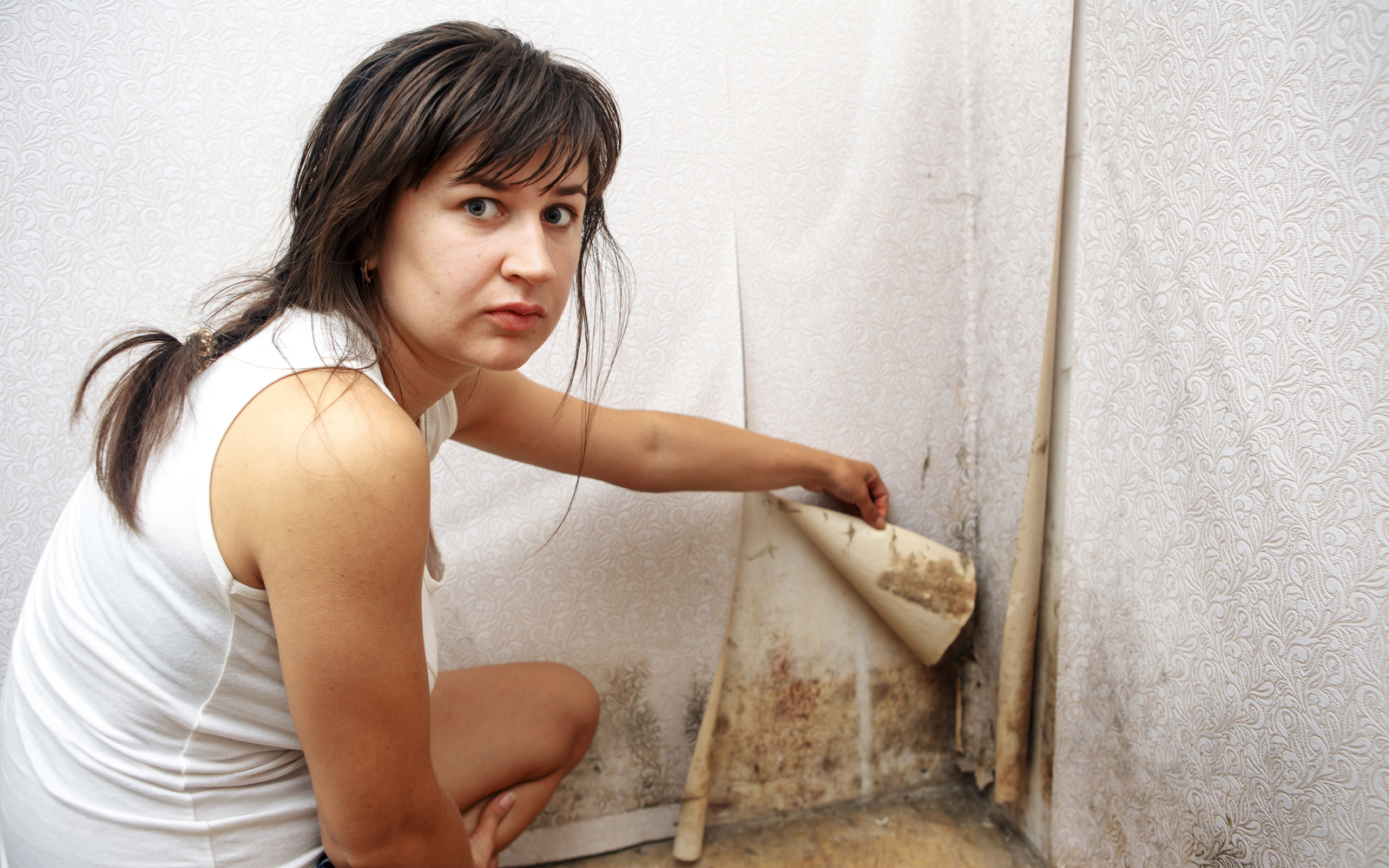 Woman pulling back wallpaper to reveal black mold
