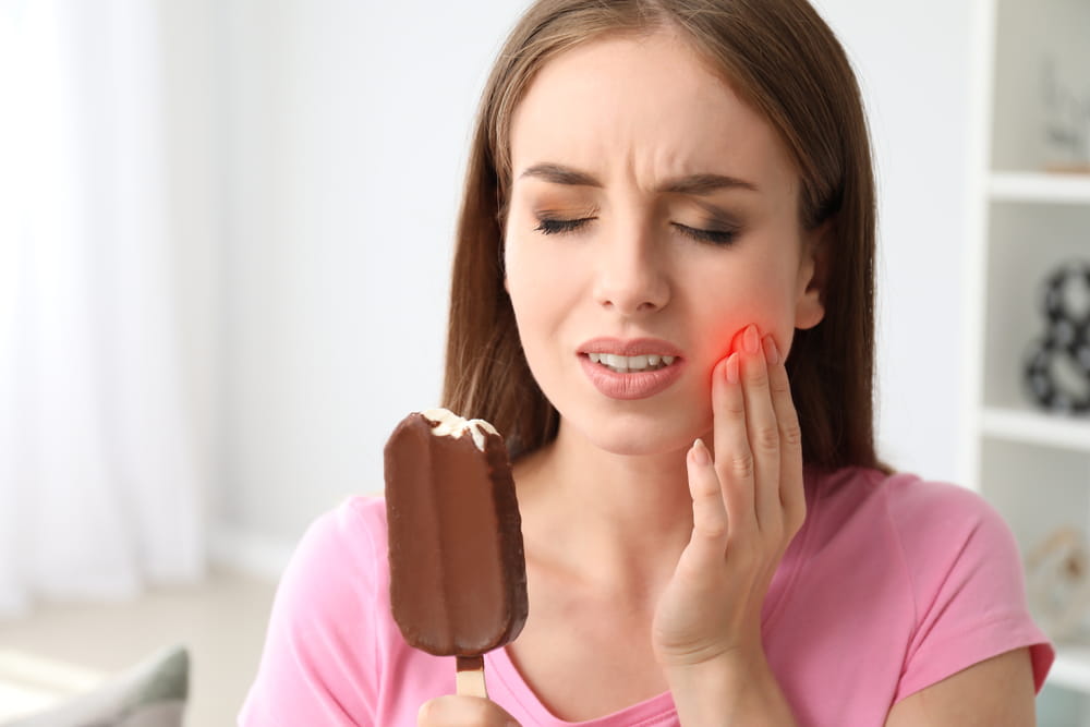 Young woman with sensitive teeth and cold ice-cream at home