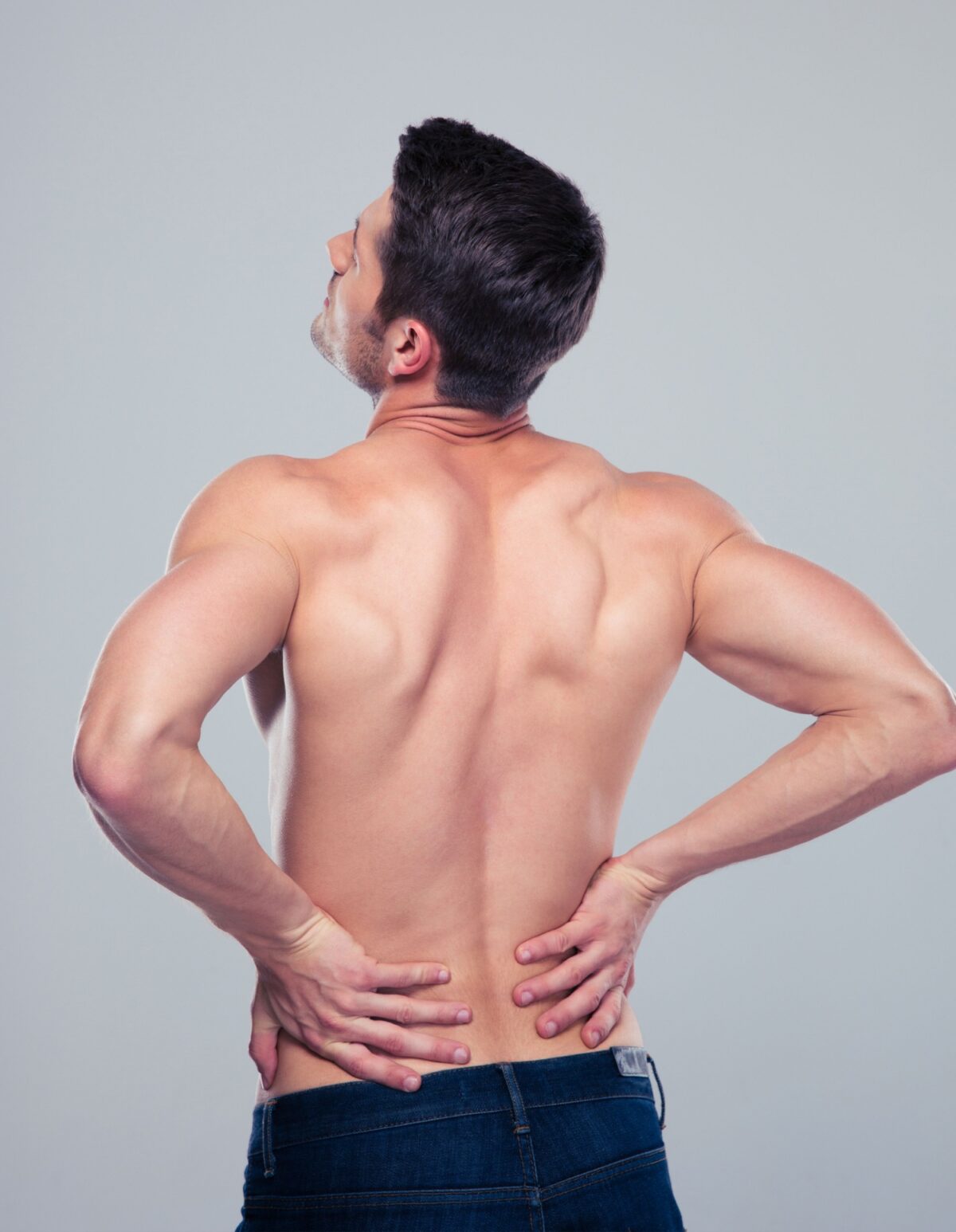 Muscular man having pain in back over gray background