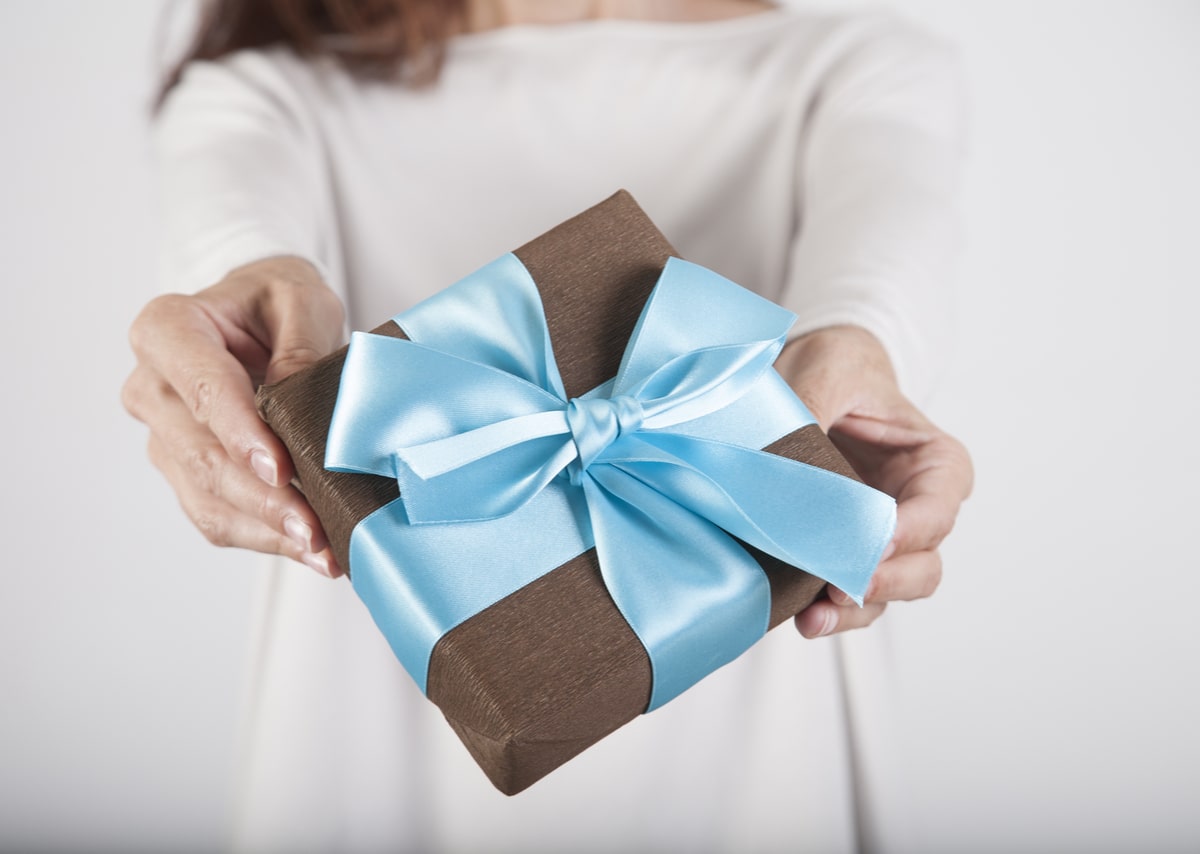 brown gift box with blue ribbon in woman blue jeans cream jersey hands over white background