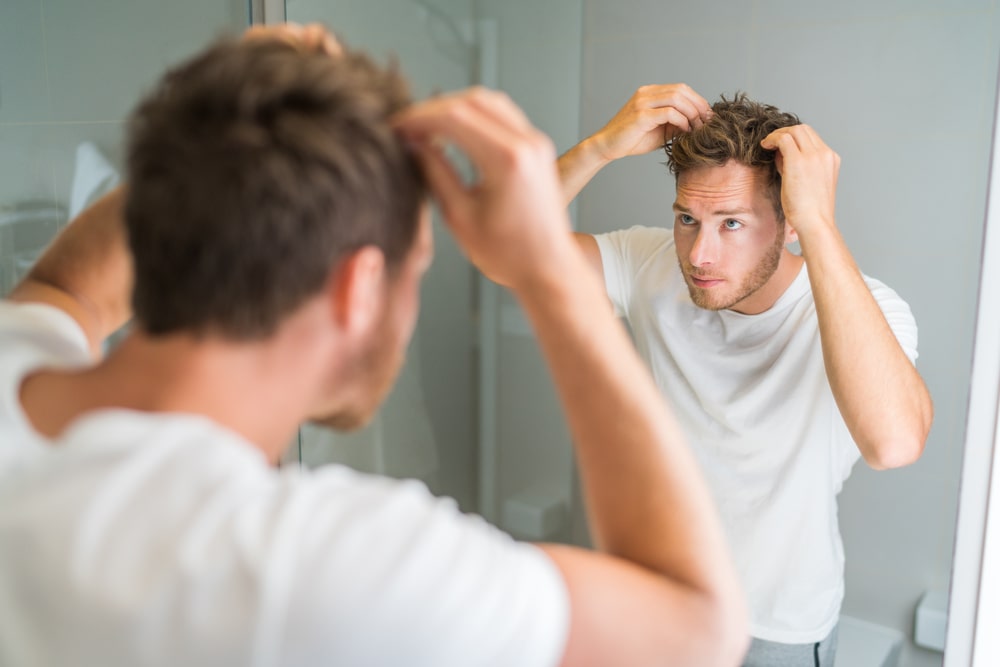 Hair loss man looking in bathroom mirror putting wax touching his hair styling or checking for hair loss problem