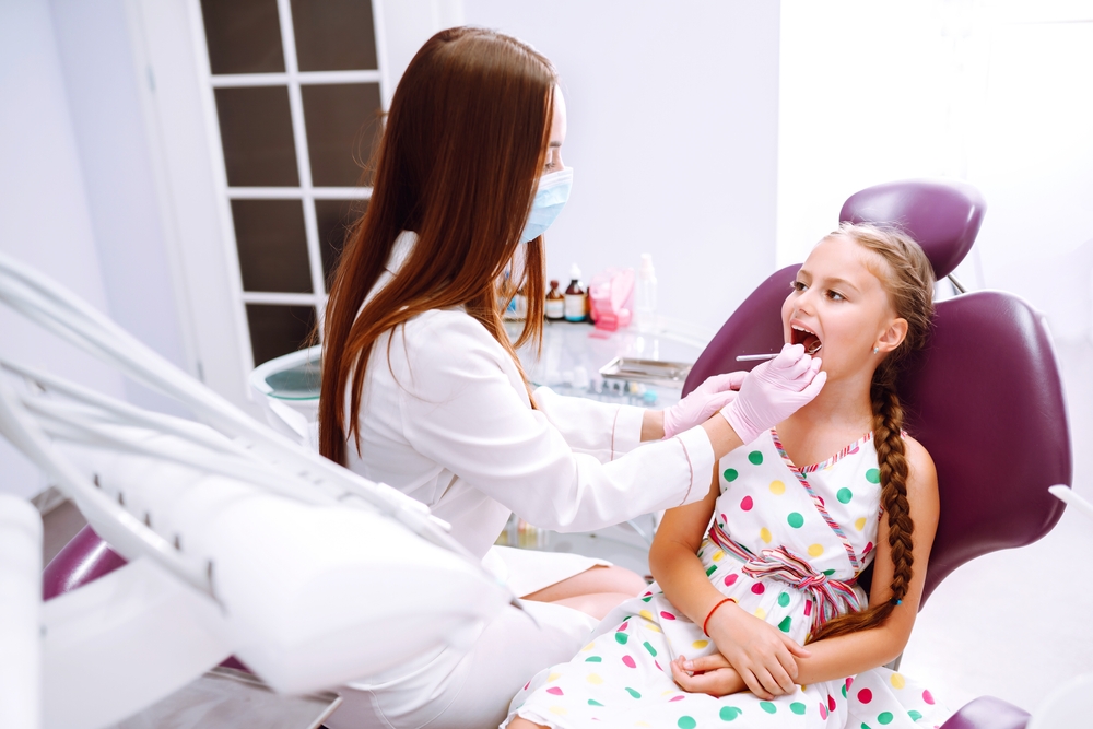Lovely little girl smiling while talking with the pediatric dentist after doing examination in a pediatric stomatology