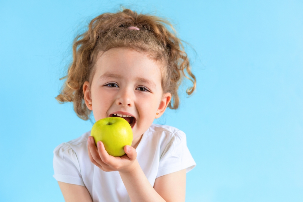 cute child smiling bites apple. nutrition for caries prevention