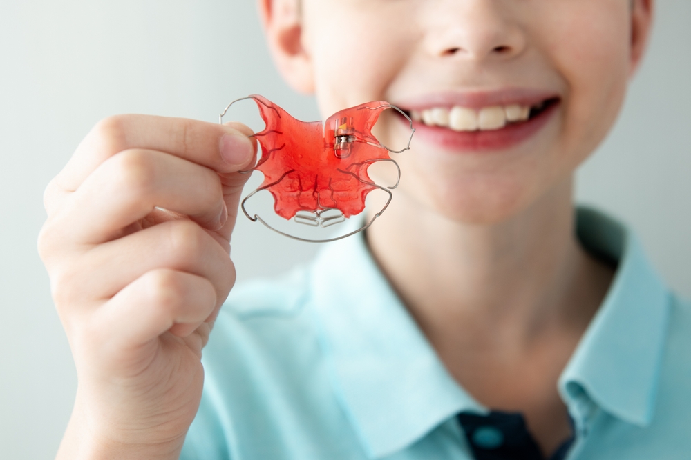 Child Holding Red Orthodontic Braces Retainer Fixer for Aligning Teeth and Expansioin Jaw