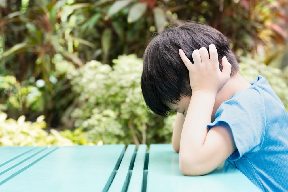 Close up of Asian autistic student child sit at table at school cover ears with hand and close eyes due to stress and anxiety