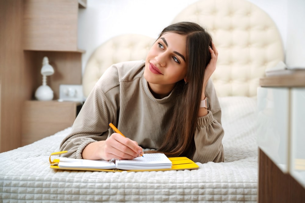 Teen girl lies on the bed and writes in a notebook, keeps a diary book, diary planner.