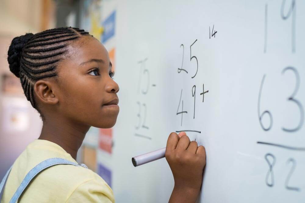 girl writing solution of sums on white board at school