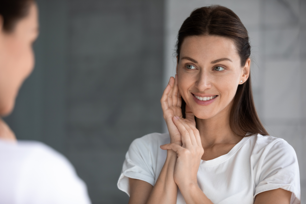 Woman looking in the mirror smiling after receiving a Skin Bleaching Treatment