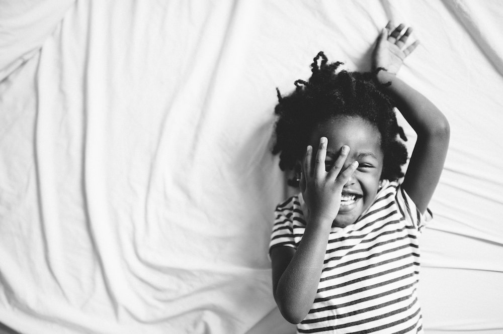 Little Girl With Hand Over Face As She Laughs On Bed