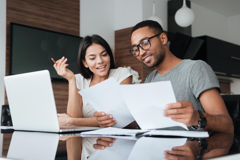 cheerful young man and woman using laptop doing paperwork