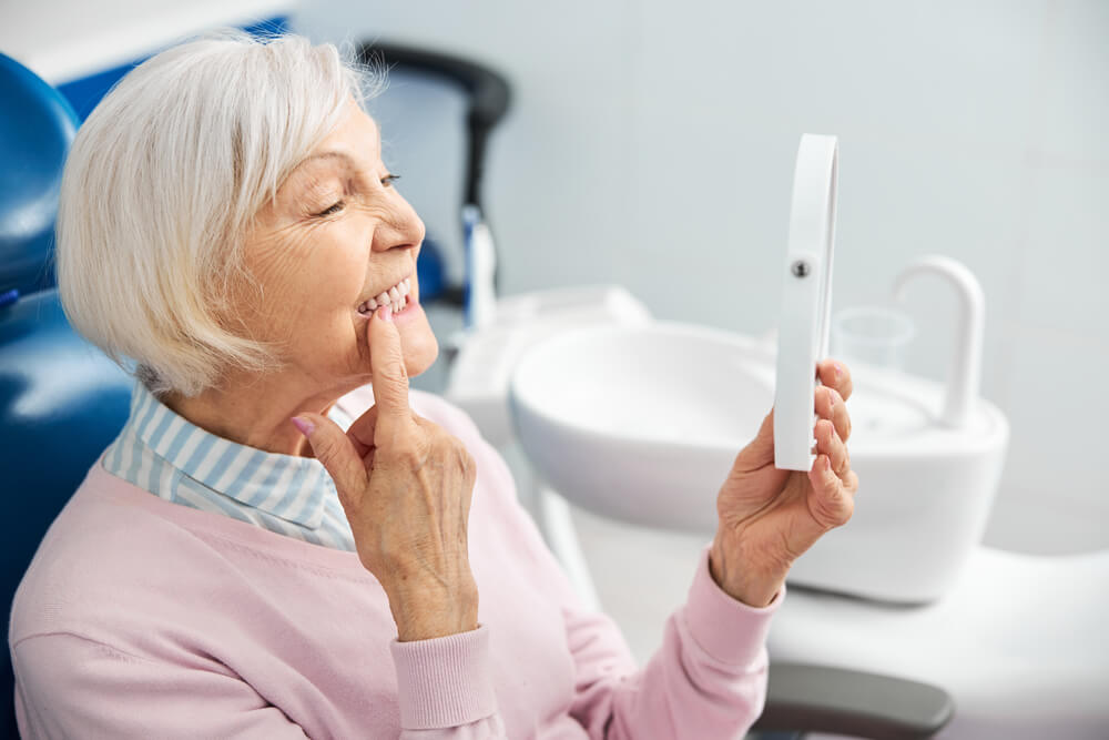 Elderly person with mirror pushing her tooth with finger