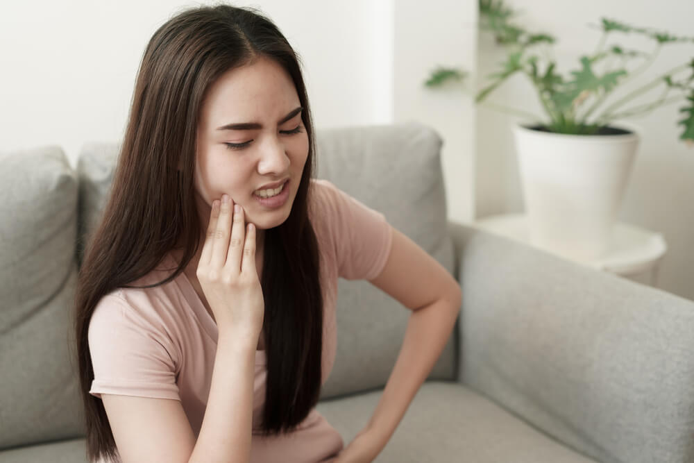 women have toothache pain while sitting on the sofa