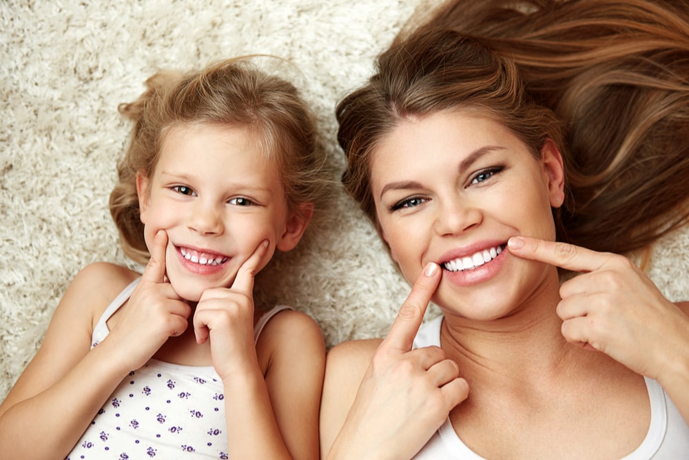 Beautiful daughter with mom showing their healthy teeth