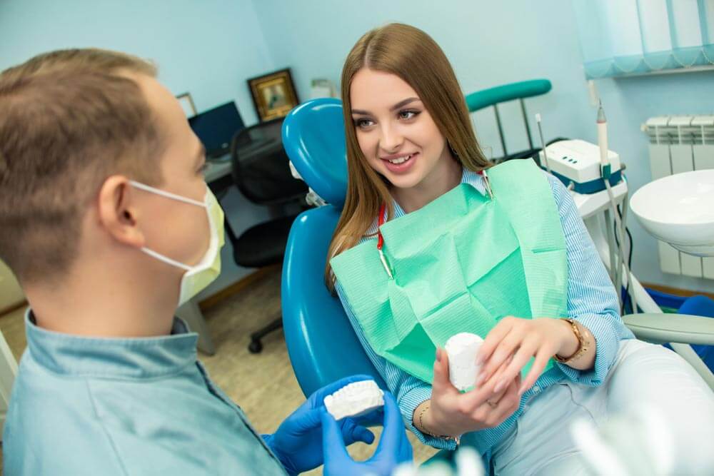 A beautiful girl is sitting in the dental chair and looking at a doctor