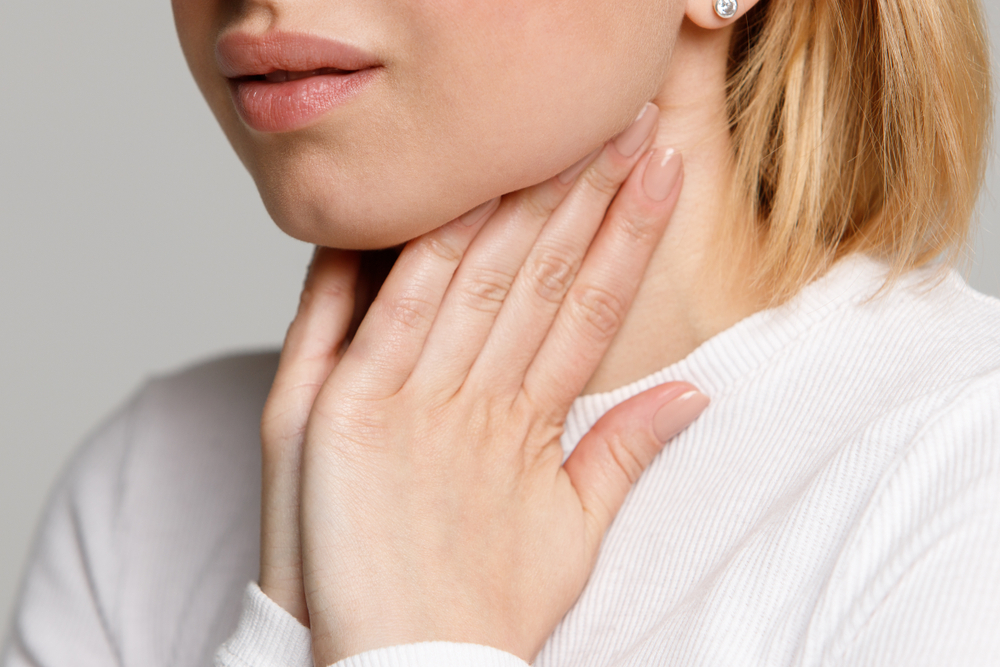 Woman holding her throat in discomfort, possibly dealing with Vocal Cord Dysfunction