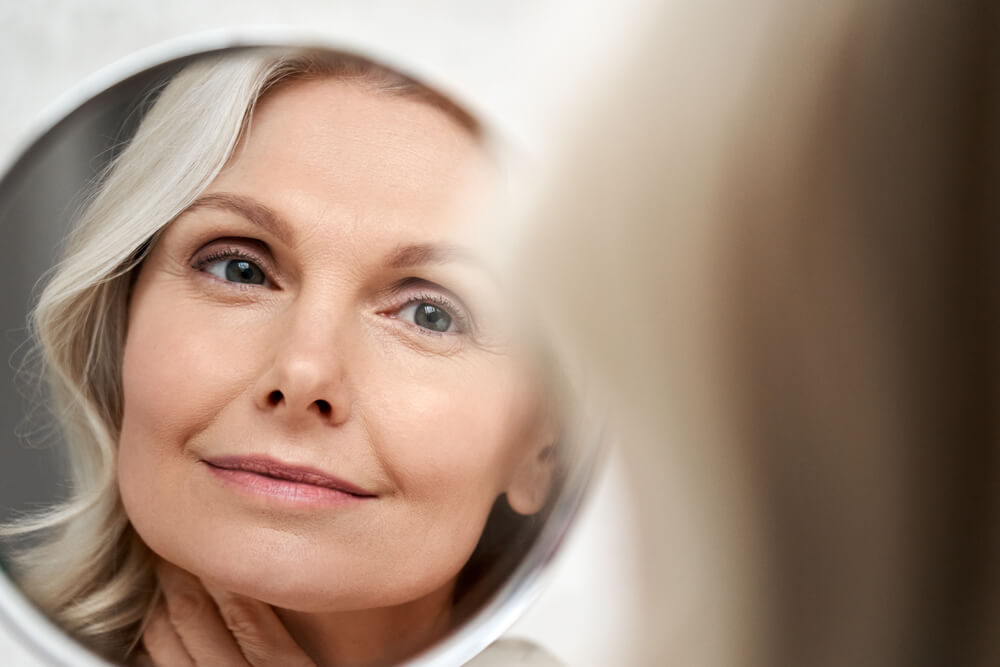 woman touching face skin looking in mirror