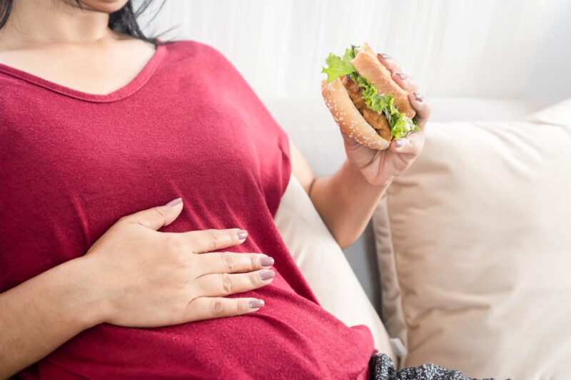 woman having stomachache or heartburn after eating burger, hand holding her abdominal
