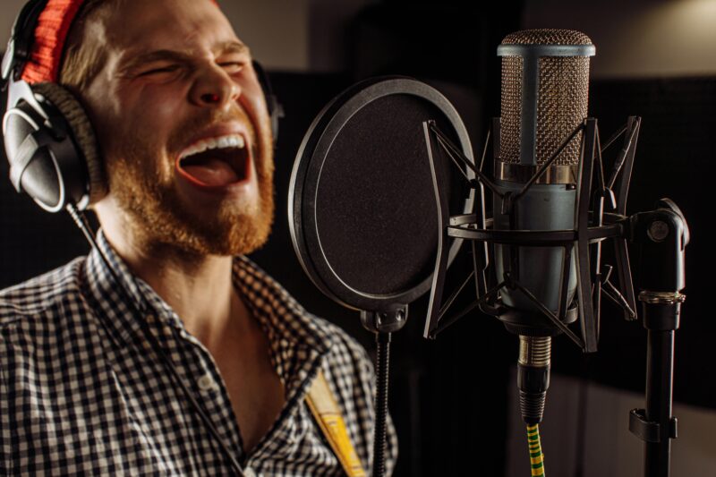 young caucasian man emotionally practice singing before music performance, concert on stage. handsome guy warms up the vocal cords in recording studio