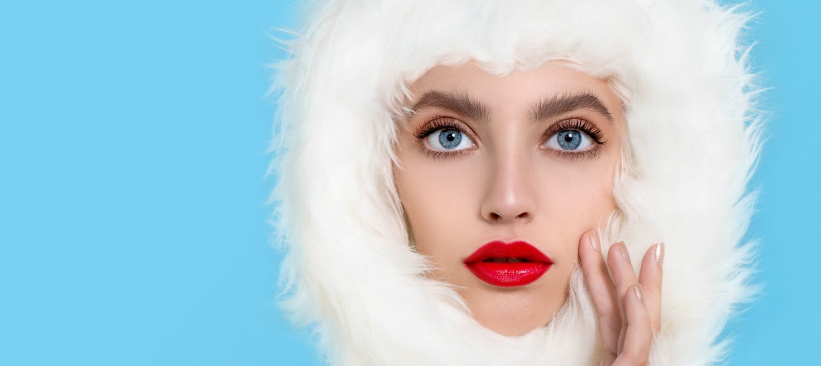 Portrait of beautiful young woman with perfect young skin, red matt lips in white fur. Model with bright scarlet color makeup and sparkled manicure. Winter seasonal beauty. Copyspace.