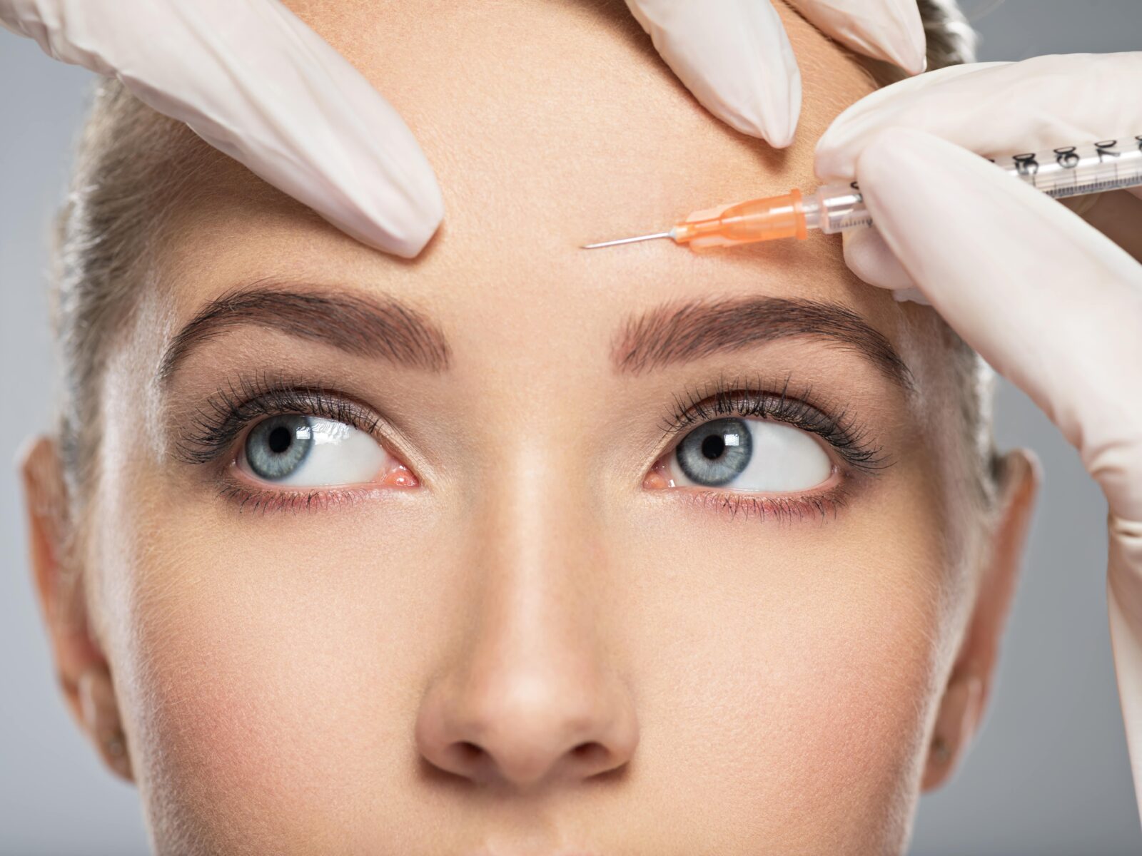 Portrait of young Caucasian woman getting cosmetic injection of botox in forehead. Beautiful woman gets botox injection in her face.